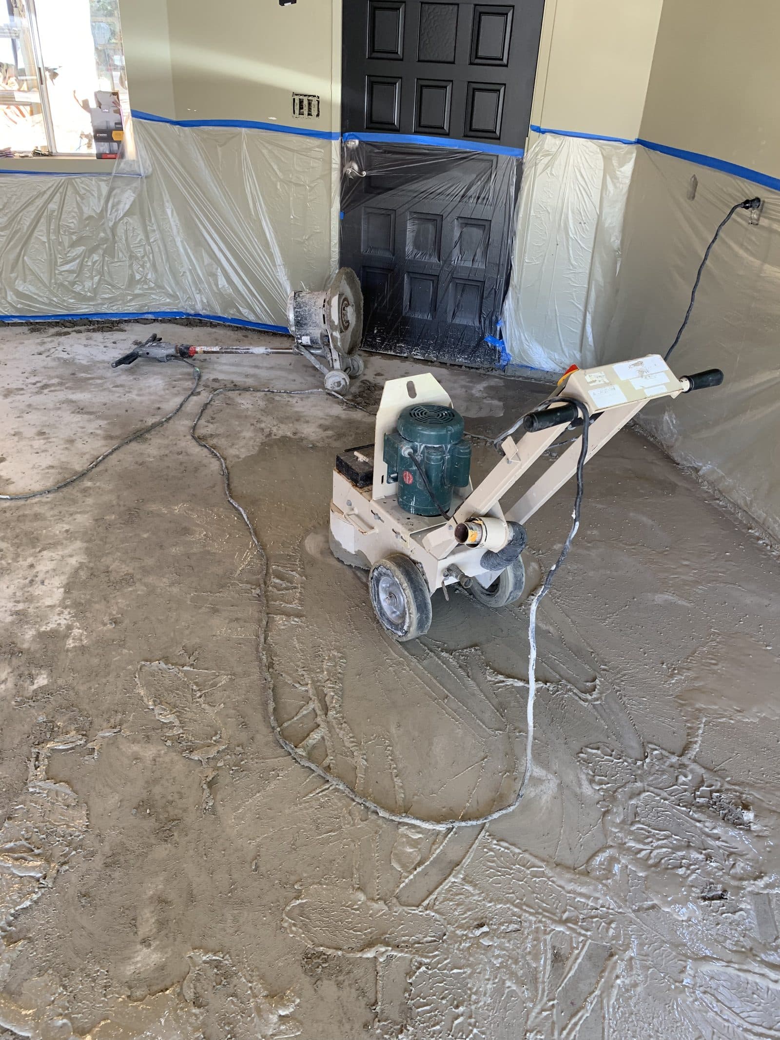 Floor grinder working a stained garage concrete slab inside plastic containment